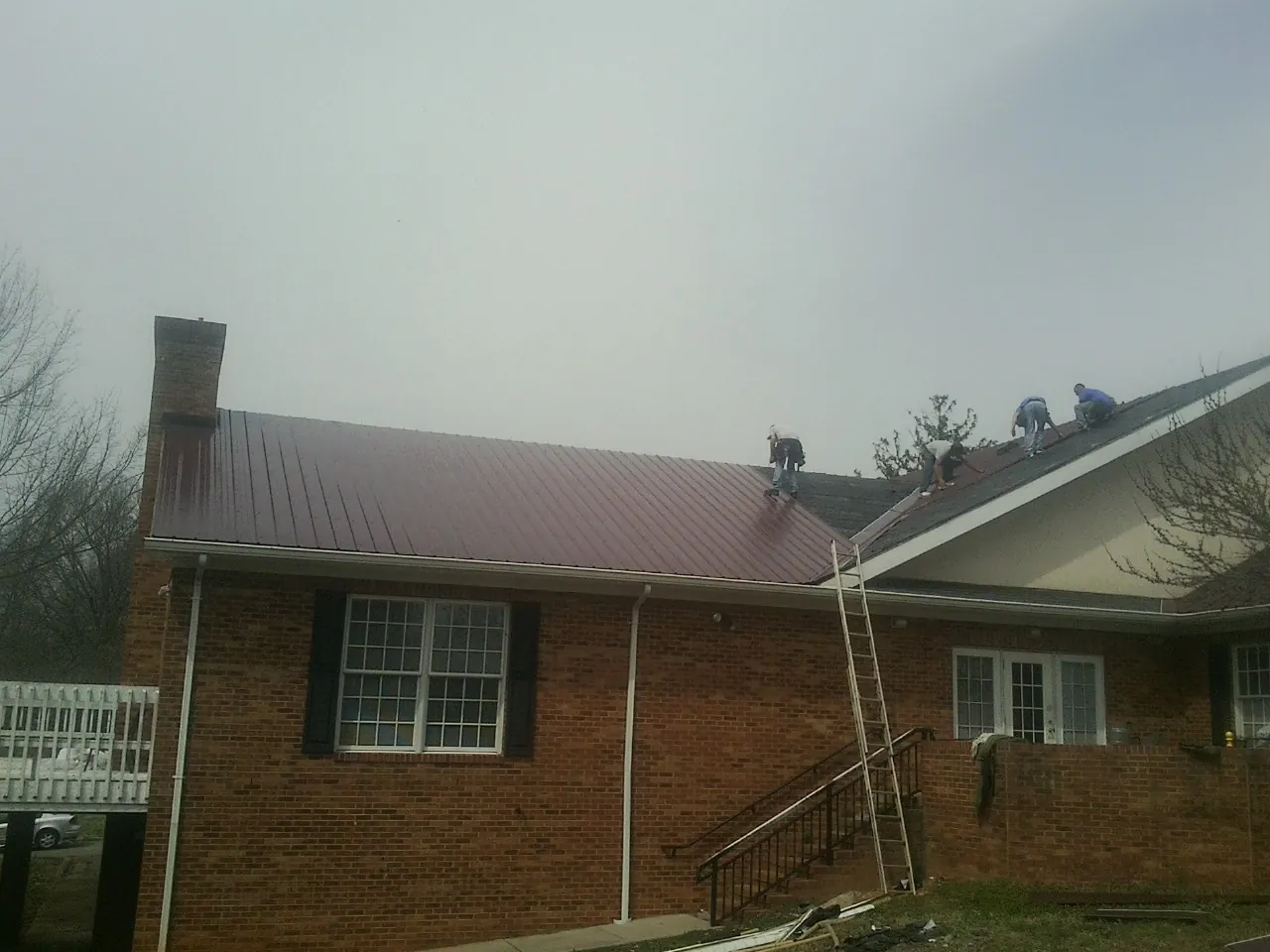 Crew setting red metal roofing panels on a brick home in Riverside